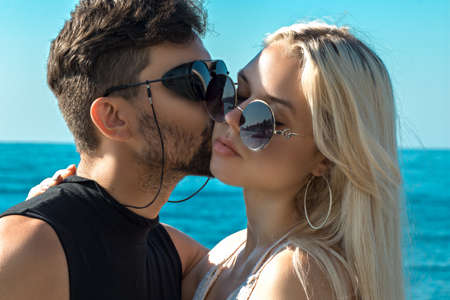 A man and a woman stand against a background of blue sky and turquoise sea. A man hugging kisses a...