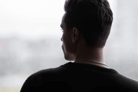 A man stands with his back in a pensive posture and looks out the windowの写真素材