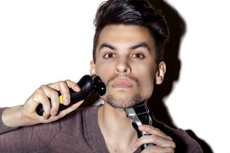Young guy shaves his face with electric razor, on white backgroundの写真素材