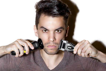 Young guy shaves his face with electric razor, on white backgroundの写真素材