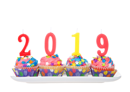 White cupcakes with rainbow colored frosting and brightly colored star candies on a rectangular plate with 2019 candles isolated on white background. Happy New Year theme.の写真素材