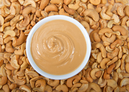 White bowl with fresh cashew butter surrounded by cashew nuts. Cashews are a good source of plant protein, contain no cholesterol and are low in saturated fat.の写真素材