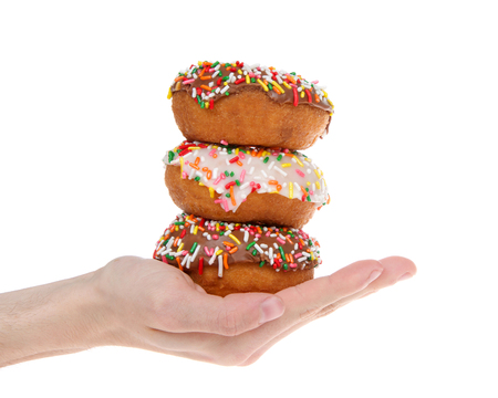 Cake donuts frosted with chocolate and vanilla frosting, rainbow candy sprinkles, stacked and held in the hand of a young male caucasian hand, isolated on white background.の写真素材