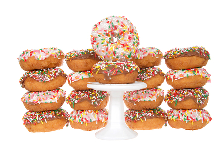 Cake donuts frosted with chocolate and vanilla frosting, rainbow candy sprinkles, stacked behind a small white pedestal with two donuts stack on top.の写真素材