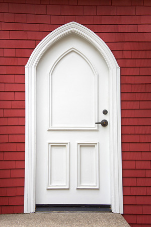 White fancy door outside with a red wood siding wall background, concrete walkway sidewalk.の写真素材