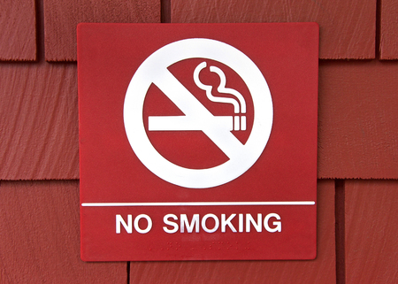 Red square sign with no smoking in white, cigarette with circle around line through as a pictorial message for non readers.の写真素材