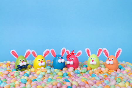 Craft Easter Bunnies made from plastic eggs standing in pastel jelly beans with a light blue background. Fun Easter line up with copy spaceの写真素材