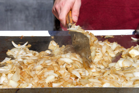 Young male hand with spatula turning chopped onions on an outside grill, grilling onions. Street vendor.の写真素材