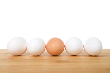 One speckled brown egg in the middle of four white eggs on a wood table with white background. Diversity concept. Copy space.の写真素材