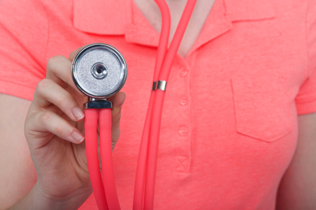 Close up on stethoscope being held out to assess listen, young woman wearing bright pink collar shirt.の写真素材