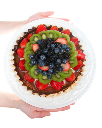Young female hands holding a white porcelain plate with fresh summer fruit tart isolated on white background. Top view flat lay vertical presentationの写真素材