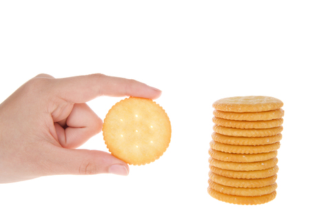 Round salted crackers stacked with young caucasian hand holding a single cracker next to pile.の写真素材
