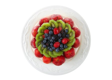 Fresh fruit on a shortbread cake with whipped cream topping on off white porcelain plate isolated on white. Flat lay, top view.の写真素材