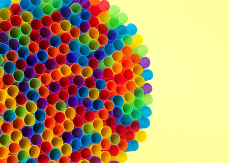 Close up of Hundreds of colorful plastic straws laying facing forwards opening towards viewer, laying on yellow surface. Many cities are now banning single use plastic straws.の写真素材