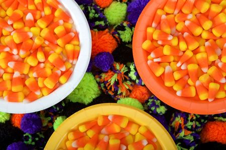 White, orange and yellow plates with candy corn and yarn balls under around below the plates in green, orange, purple and black. Festive Halloween party flat lay top viewの写真素材