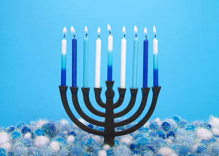 a nine-branched menorah (also called a Chanukiah or Hanukiah) burning candles to celebrate Hanukkah against a light blue background with light and dark blue and white shiny yarn balls underneath.の写真素材