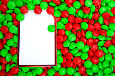 Background of red and green candy coated chocolate treats with white card vertically on the left blank for your text. Traditional Christmas holiday colors.の写真素材