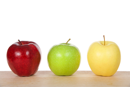 One red, green and yellow apples on a light wood table isolated on white backgroundの写真素材