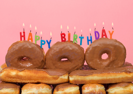 Close up on Chocolate covered donuts stacked with Happy Birthday candles burning on top,  pink background. Donut lovers birthday cakeの写真素材