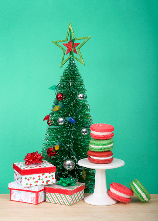 Christmas holiday style macaron cookies stacked on a pedestal and laying on wood table with light green background with colorful presents and small Christmas tree. Vertical formatの写真素材