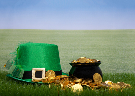 Pot of gold spilling over onto green grass, Leprechaun hat laying next to it, green grass field off to the skyline. Copy spaceの写真素材