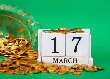 Close up on wood blocks showing calendar date March 17th, Saint Patrick's Day, sitting on green background, leprechaun hat with gold coins spilling out next to blocks.の写真素材