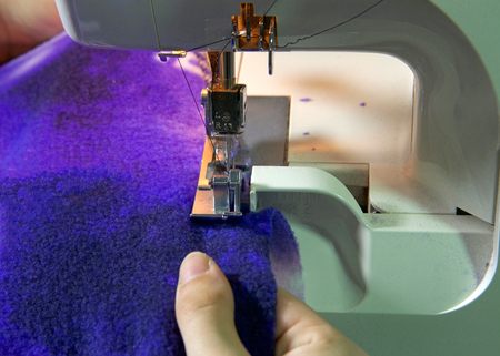 Female hands serging flannel blanket material white sewing machine. Serging raw edges is helpful...