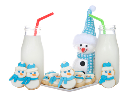 Snowmen sugar cookies with blue scarfs and fluffy blue and white hats on a plate with bottles of milk green and red straws. More snowmen cookies standing next to glasses of milkの写真素材