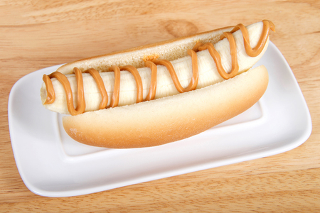 Banana with peanut butter in a hot dog bun served on a white rectangular plate served on a wood table. Top view from an angleの写真素材
