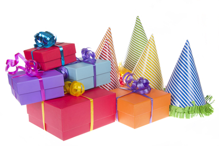colorful present boxes with ribbon stacked asymetrically and randomly with party hats next to them isolated on white backgroundの写真素材