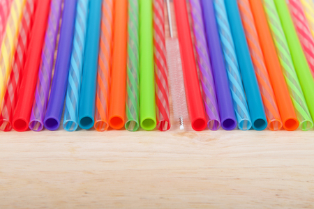 Row of colorful plastic and silicone reusable straws with cleaning brush in the middle laying on light wood table, viewed from above in front. Ecologically friendly.の写真素材