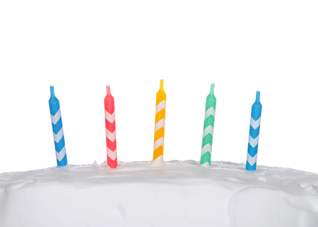 Colorful striped birthday candles on white frosted cake isolated on white backgroundの写真素材