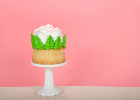 Large cup cake with giant frosting rose sitting on white pedestal on wood table. Simple design with copy space for Mother's Day, Valentine's Day, Quinceanera or birthdayの写真素材