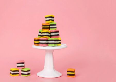 Colorful fancy candy licorice squares piled on a tiny pedestal with several at the base of it on pink background with copy space.の写真素材