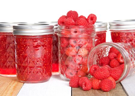 Whole fresh raspberries in open mason jars, one spilling fruit on table in front of full home made...