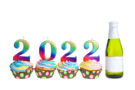 Colorful rainbow frosted vanilla cupcakes sitting in a row with 2022 candles on top next to a small bottle of wine, blank label. Isolated on white.の写真素材