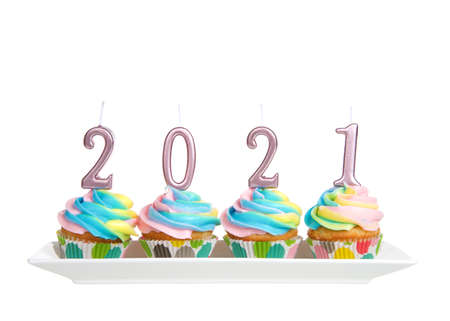 Colorful rainbow frosted vanilla cupcakes sitting in a row on a rectangular porcelain plate with 2021 candles on top. Isolated on white.の写真素材
