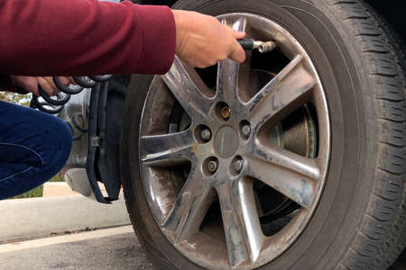 Close up of an older woman, female hands using automated air pump to inflate car tire with low pressure.の写真素材