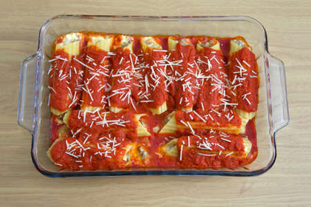 Freshly baked stuffed manicotti covered in marinara sauce and sprinkled with parmesan cheese sitting on a wood table.の写真素材