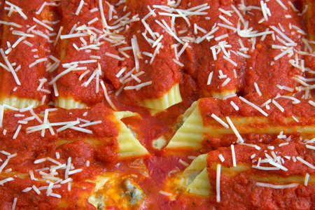 Close up on freshly baked stuffed manicotti covered in marinara sauce and sprinkled with parmesan cheese.の写真素材
