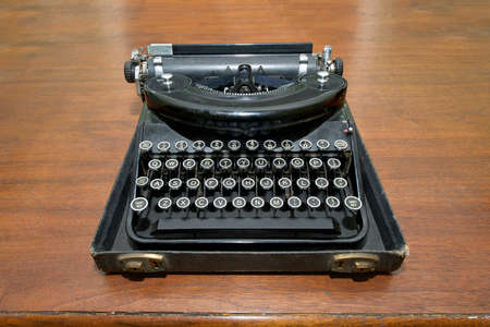 Antique type writer sitting in the lower half of carrying case on an old dark wood table. Vintage.の写真素材