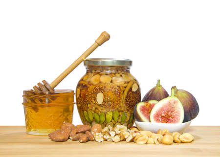 Jar of nuts and fruit preserved in a jar of honey. Ingredients Pistachios, walnuts, peanuts, almonds and figs on a light wood table isolated on white.の写真素材