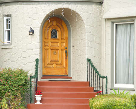 Wooden door rounded at top on front of old house with red stairs leading to entry. Poinsettia plants potted on stairwayの写真素材