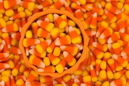 Top view of a small porcelain pumpkin bowl filled with candy corn spilling over onto a background of...