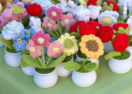 Close up on many beautiful crochet flowers in small white plastic pots on a green table. Hand crafted.の写真素材
