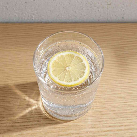 Glass of water with lemon on wooden table and gray wall background.