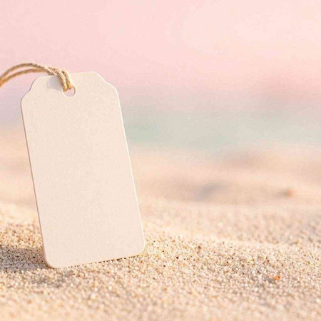 Blank paper price tag on the beach sand with copy space.