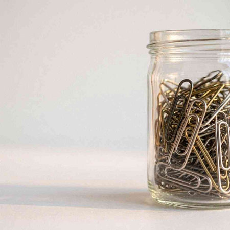 Paper clips in a glass jar on a white background. Copy space.