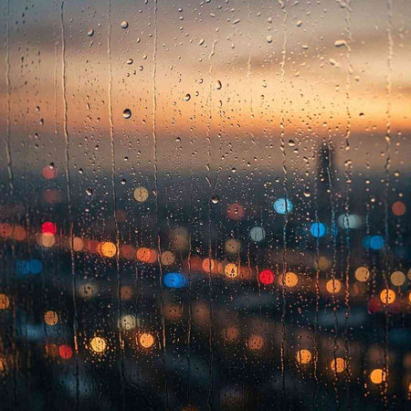 Rain drops on the window. Blurred city view at sunset.