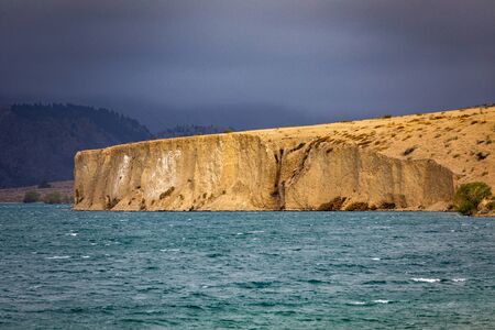 A Stormy Lake At Aviemore In New Zealand. This CLiff Side Is Bathed In Light As The Clouds Roll In
